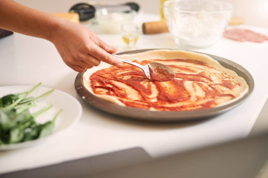spreading sauce on pizza base